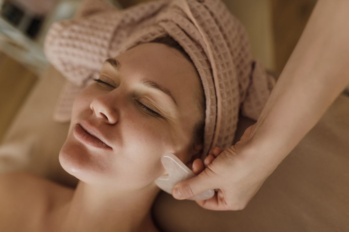 Lifting facial casero: fotografía editorial de mujer recibiendo masaje facial con herramienta gua sha