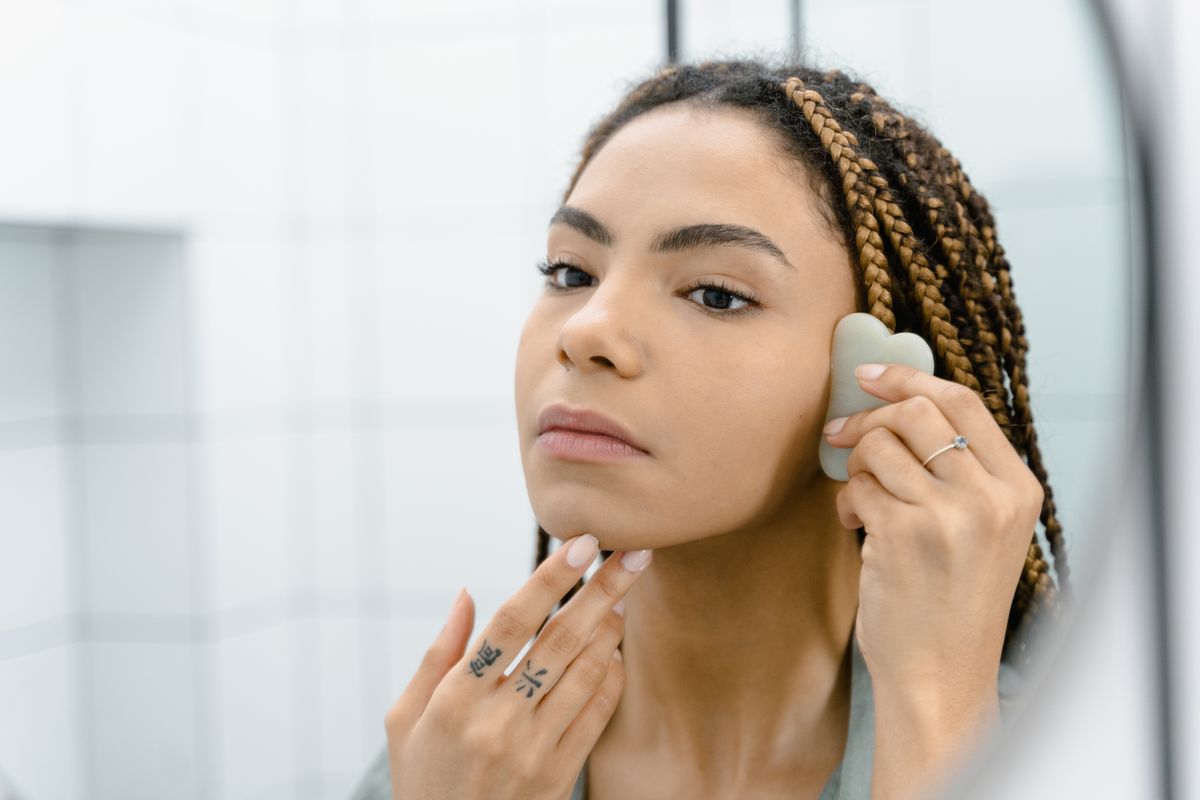 Masaje lifting facial: fotografía editorial de mujer realizando masaje facial con una piedra gua sha